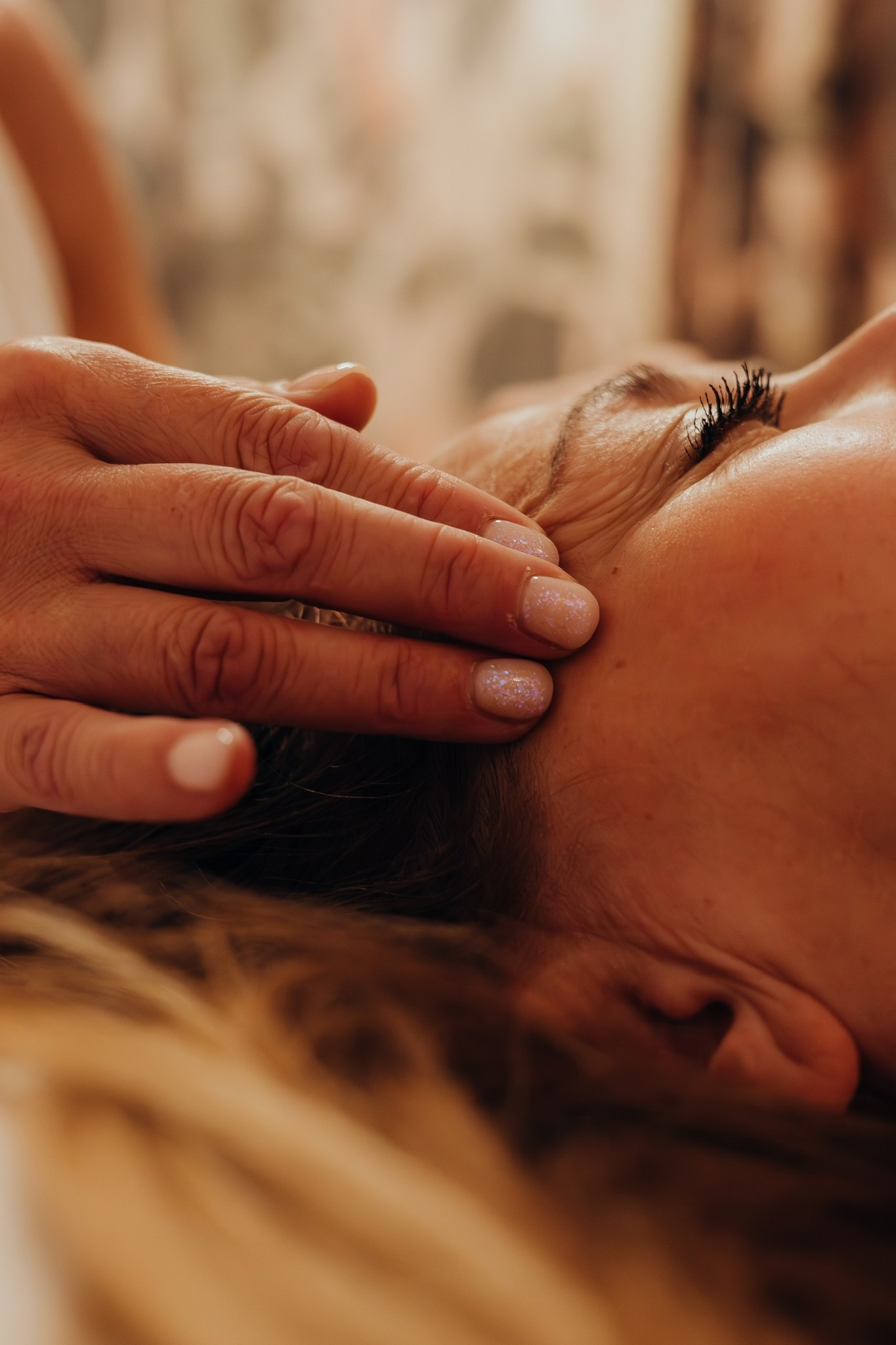 Lina’s hands gently touching a client’s forehead and temple area